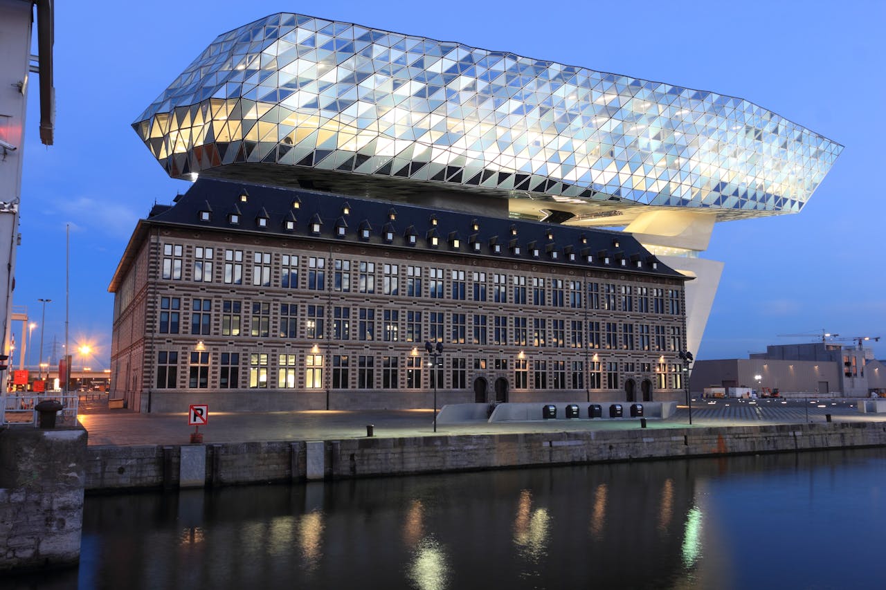 Stunning view of Antwerp's modern Havenhuis reflecting on the river at twilight.